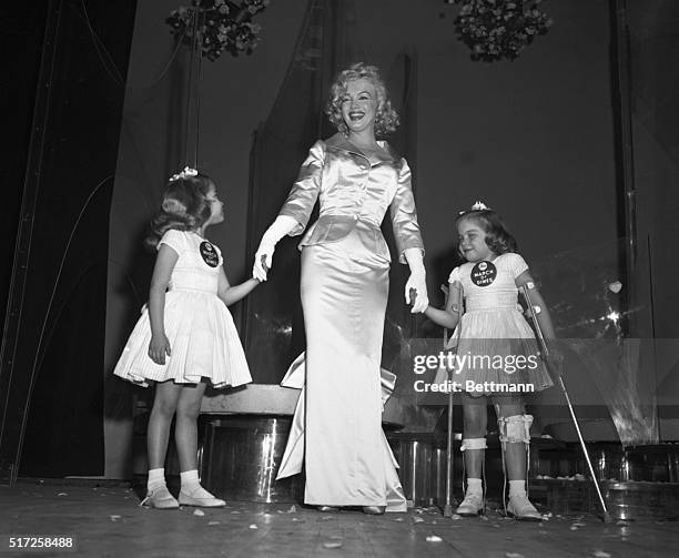 Actress Marilyn Monroe Miller is kissed by the march of dimes poster twins, six-year-old Lindy and Sandy Sue Solomon at today's annual March of Dimes...