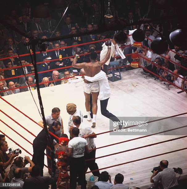 Handlers rush in to embrace the jubilant Cassius Clay after he won the heavyweight boxing title when champ Sonny Liston, seated in his corner,...