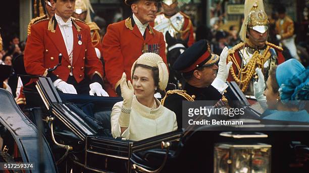 Queen Elizabeth II of England and Prince Philip wave to crowds as they ride in open carriage to investiture of son Prince Charles as Prince of Wales...