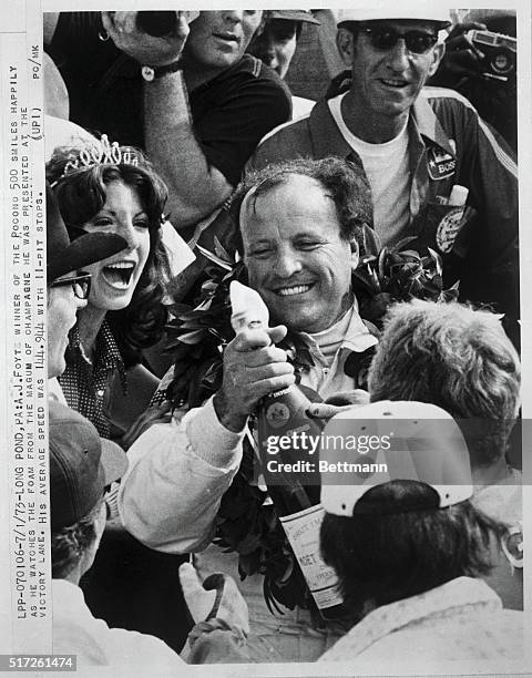 Foyt, winner of the Pocono 500, smiles happily as he watches the foam from the magnum of champagne he was presented at the victory lane. His average...