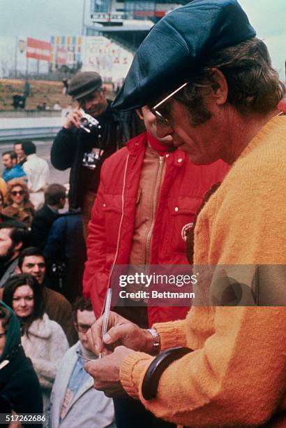 Le Mans, France: Actor Steve McQueen, wearing a cap and sunglasses, signs autographs for his fans at the Le Mans track. Steve, after racing in the...