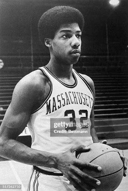 Portrait of Julius Erving, basketball player for University of Massachusetts, shown from the waist-up, in uniform, holding basketball.