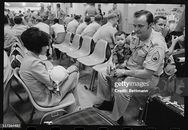 Unidentified American sargeant with his Vietnamese wife and two kids relax at Camp Alpha 3/28 among a crowd of American GI's scheduled to leave for...