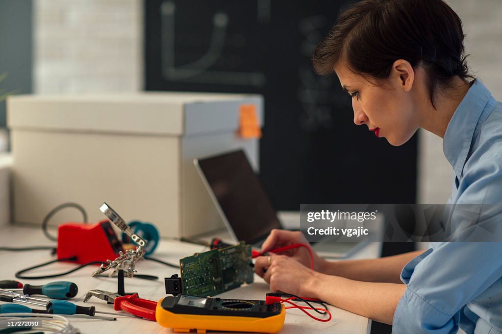 Woman Testing circuit board in her office.