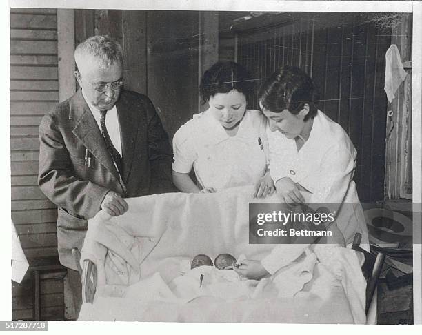 Nurse, relatives and neighbors are helping keep the "Dionne quintuplets" born in Corbeil, Ontario alive, as shown here. Two nurses administering milk...