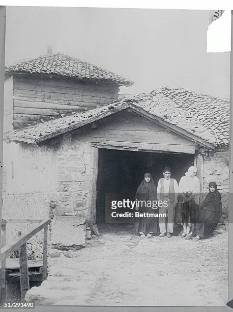 Rumania: Photo shows Queen Marie of Rumania in national garb pointing with some of her subjects in front of their unpretentious home at Balcic. Note...