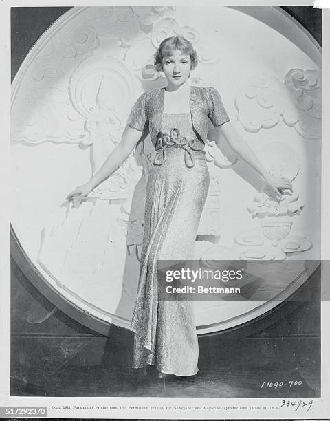 Claudette Colbert, Paramount star, selects a dinner gown of brocaded silver lame. The brief little jacket makes the gown ideal for both dining and...