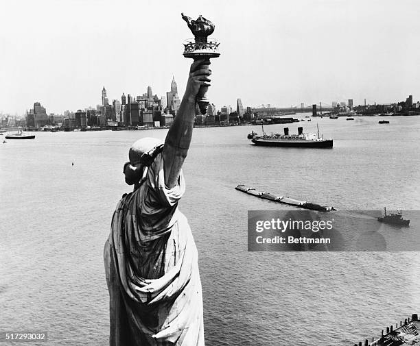New York: A striking view of New York Harbor and the magnificent skyline of lower Manhattan, made from behind the Statue of Liberty, who stands with...