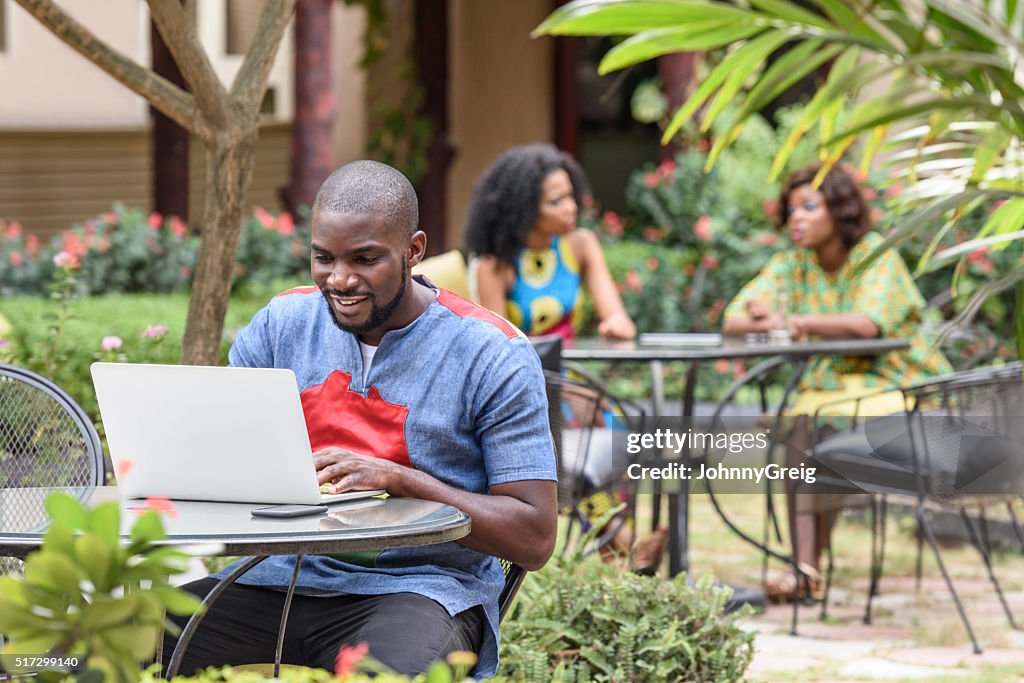 Young African man using laptop in cafe garden using