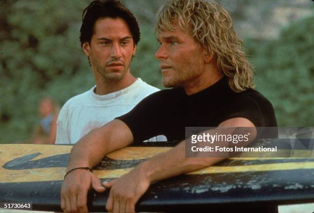Lebanese-born American actor Keanu Reeves and American actor Patrick Swayze stand on a beach as Swayze holds a surfboard during the filming of the...