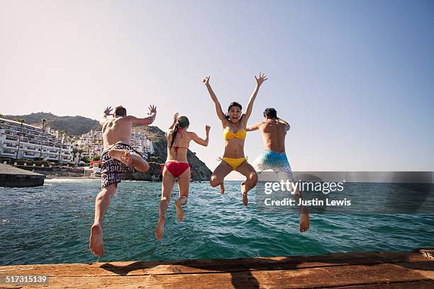 four swimsuited friends leap from dock - catalina island stock-fotos und bilder