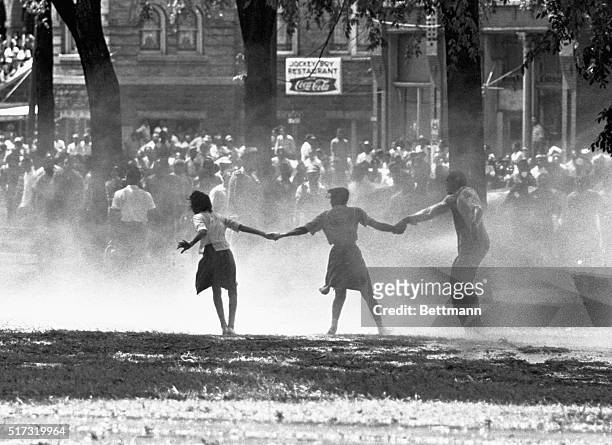 Three demonstrators join hands to build strength against the force of water sprayed by riot police in Birmingham, Alabama, during a protest of...