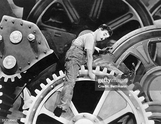 Silent film comedian Charlie Chaplin exagerates movements and actions sitting on gears in the motion picture Modern Times in 1936.