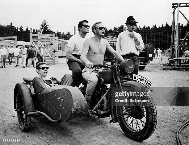 Between takes on the film The Great Escape, Steve McQueen in the driver's position on a motorcycle with James Garner behind him and James Coburn in...