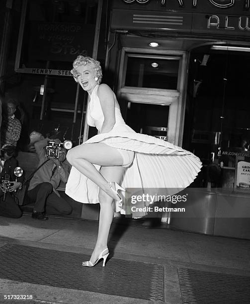 Film star Marilyn Monroe poses over a Manhattan subway grate as the wind blows her white dress up. Photographers capture the moment on camera, which...