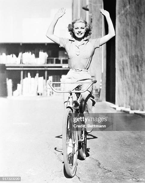 Ginger Rogers holds her hands up high while riding a bicycle on the RKO Radio Pictures lot on July 1, 1936.