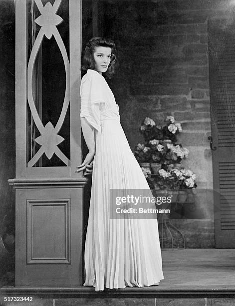 Actress Katharine Hepburn in various full length poses and costumes. Here, Hepburn poses seductively in a door frame in a long white dressing gown...