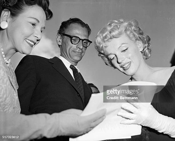 While her husband, playwright Arthur Miller looks on, actress Marilyn Monroe signs an autograph for a fan.