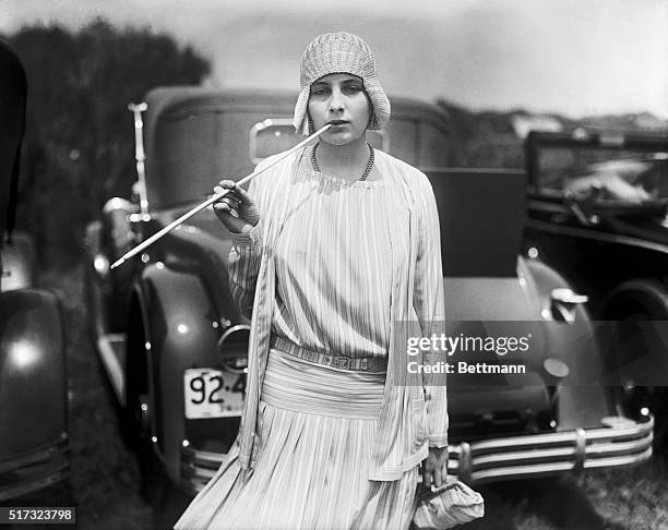 Nadeja De Braganza, daughter of Princess Miguel De Braganza, smokes a cigarette from a long cigarette holder while standing near parked cars. June...