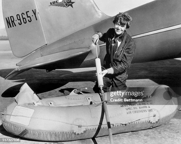 Amelia Earhart is shown here as she inflated the tiny rubber life raft that was part of the equipment of her "flying laboratory," during preparation...