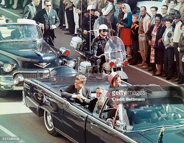 President John F Kennedy, First Lady Jacqueline Kennedy, Texas Governor John Connally, and others smile at the crowds lining their motorcade route in...