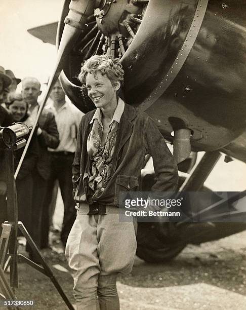 Amelia Earhart , American aviator, smiling as she stands near her plane.