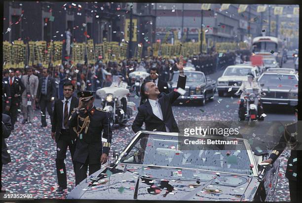Miguel de la Madrid , president of Mexico from 1982 to 1988, waves triumphantly from an open-topped car during his inaugural motorcade in Mexico City.