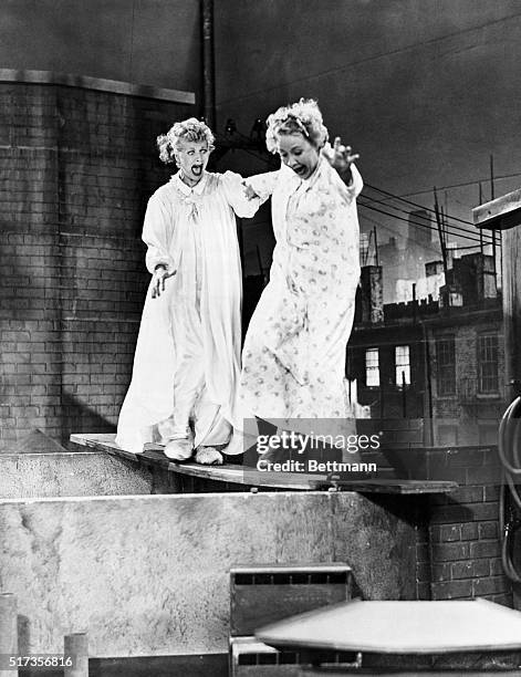 Lucy and Ethel, portrayed by Lucille Ball and Vivian Vance, cross roof tops on a wobbly plank during a scene on I Love Lucy.