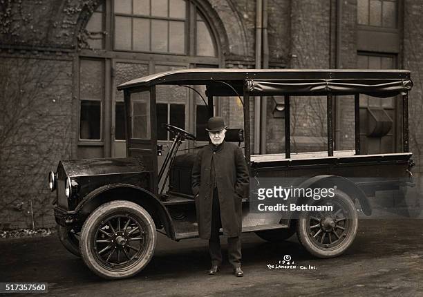 Portrait of American inventor Thomas Edison standing beside an electrically-driven automobile which he helped develop. Photograph, 1921.