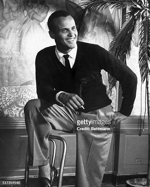 Portrait of Jamaican-American musician, actor, and Civil Rights activist Harry Belafonte as he poses, one foot on a chair and a cigarette in his...
