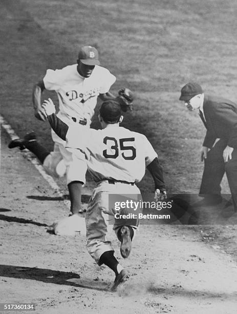 Jackie Robinson likes to beat the batter to first base when he fields a ball down his way. He's shown here outrunning Yogi Berra, Yank catcher, in...