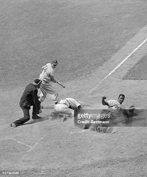 Brooklyn Dodgers' Jackie Robinson is shown sliding hard to steal home but, he is tagged out by Rube Walker of the Chicago Cubs.