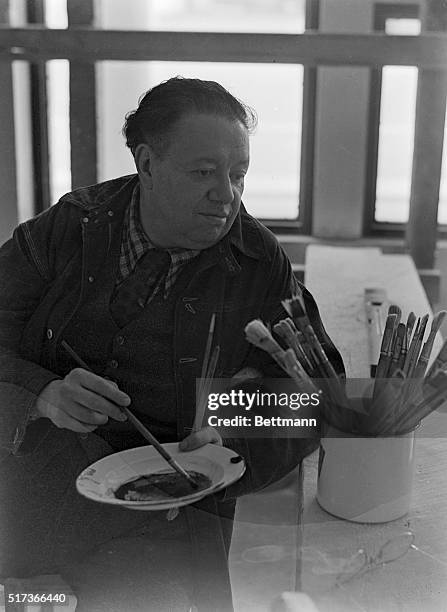 This photo shows the Mexican painter Diego Rivera, , seated, as he mixes in a plate with a paintbrush.