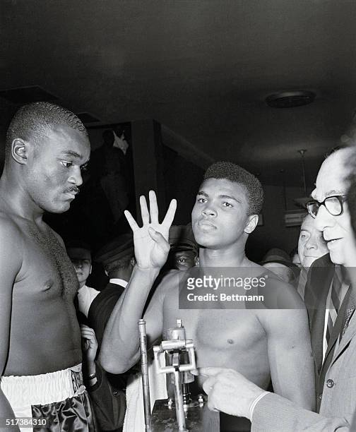 Weighing in in the lobby of New York's Madison Square Garden March 13th, Cassius Clay holds up four fingers to underscore his prediction that he'll...