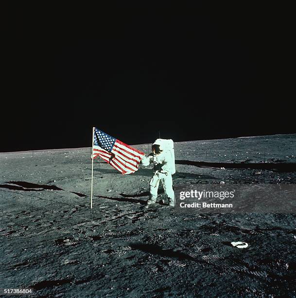 Space Center, Houston: An Apollo 12 astronaut unfurls a plastic United States flag on the moon upon landing November 19th. Commander Charles Conrad...