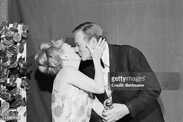 Los Angeles: Actor John Wayne presents the Cecil B. DeMille Award to actress Joan Crawford as the two meet with the press during the 27th Golden...