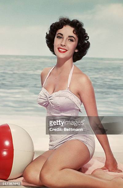 Elizabeth Taylor poses in a swimsuit with a beach ball.