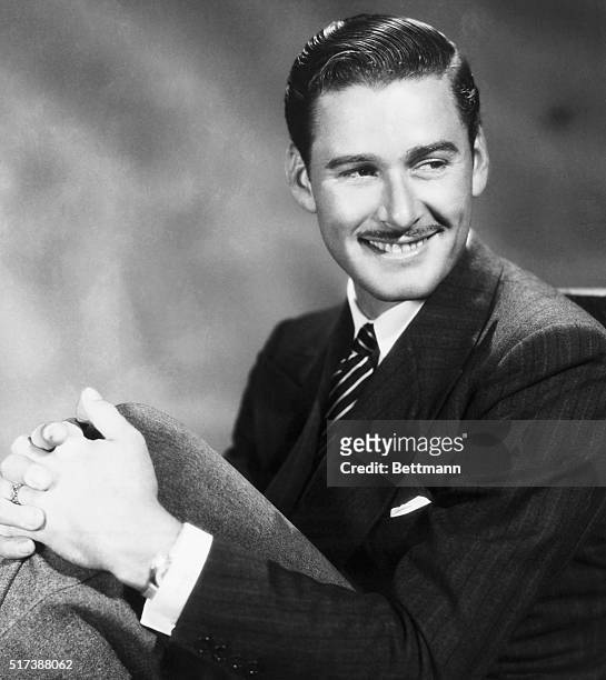 Portait of actor Errol Flynn , with his hands around his knees. Undated photograph.