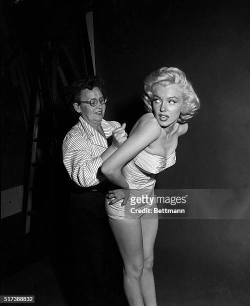 Wardrobe assistant helps actress Marilyn Monroe into a strapless swimsuit for Independence Day activities.