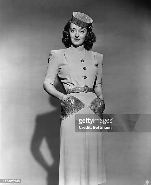 Bette Davis, who co-stars with George Brent in Warner Brothers' "The Great Lie," contrasts a simply-tailored, beige crepe street dress with snakeskin...