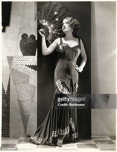 Norma Shearer as she appears in the 1930 MGM drama, "Let Us Be Gay." She is shown here wearing a full-length evening gown and holding a sequined fan.