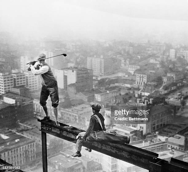 Playing golf in mid-air: Stunts. A cigarette smoking golfer and his caddy teeing off on the girder of a building under construction high over an...