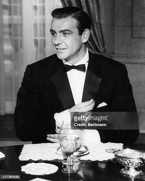 Sean Connery, in a scene from Goldfinger, adjusts a cuff of his tuxedo while dining with M and the Prime Minister.