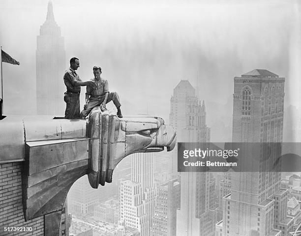 Man lights a fellow worker's cigarette as they take a break on a Chrysler Building gargoyle.