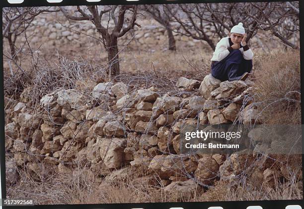 Majdel Shams, Israeli-Occupied Golan Heights. A young Druse Arab boy sits quietly on a stone wall surrounded by barbed wire as he looks out over...