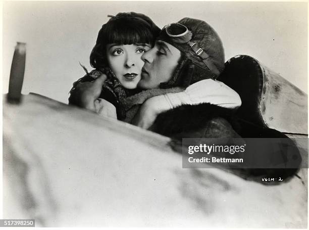 Photo shows Gary Cooper and Colleen Moore in a publicity handout from the movie "Lilac Time." They are shown embracing in the cockpit of an airplane.