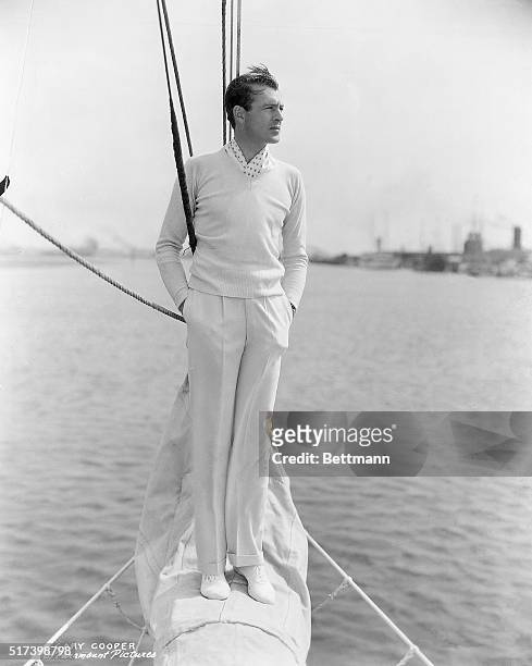 Paramount Pictures publicity portrait of Gary Cooper. He is shown full-length, standing on the prow of a sailboat. Photograph, circa 1939.
