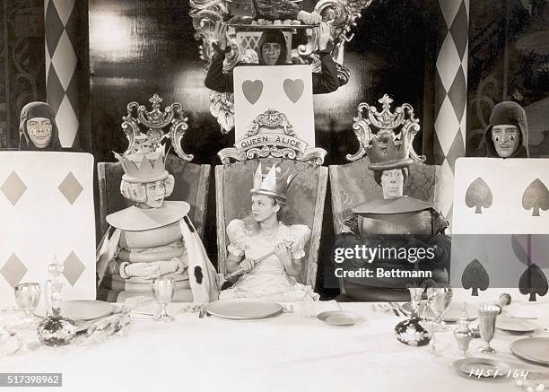 Picture shows a scene from the movie, "Alice in Wonderland", written by Lewis Carroll. Alice is shown seated between the two chess pieces in a chair...