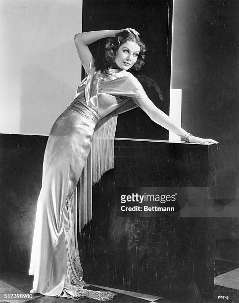 Shimmering white satin forms effective draping for Loretta Young, MGM player, who is smartly attired for the evening affair.