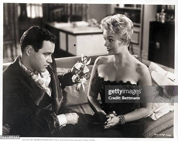 Picture shows actor, Jack Lemmon, seated on a couch and handing actress, Kim Novak, a rose in a scene from the movie, "Phifft".